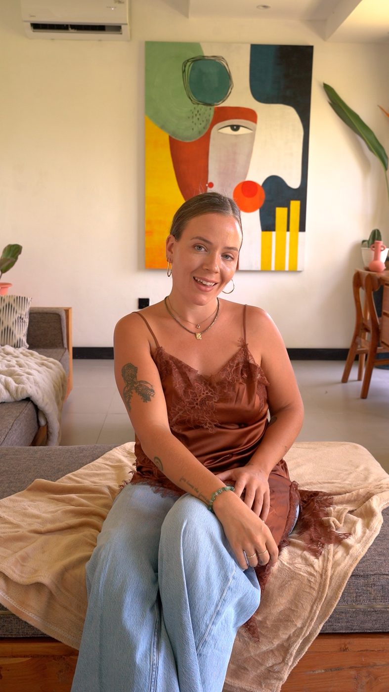 Heather sitting on a bed in front of a colourful painting