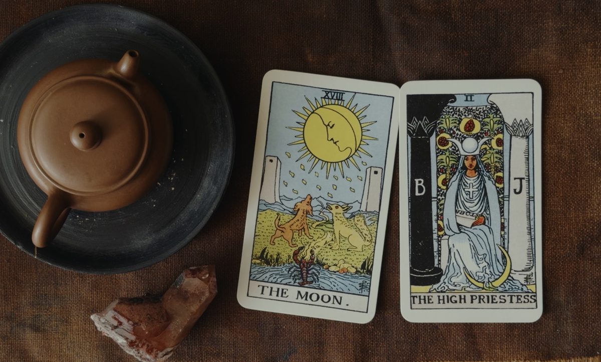 The Moon and The High Priestess tarot cards beside a clay teapot and a crystal